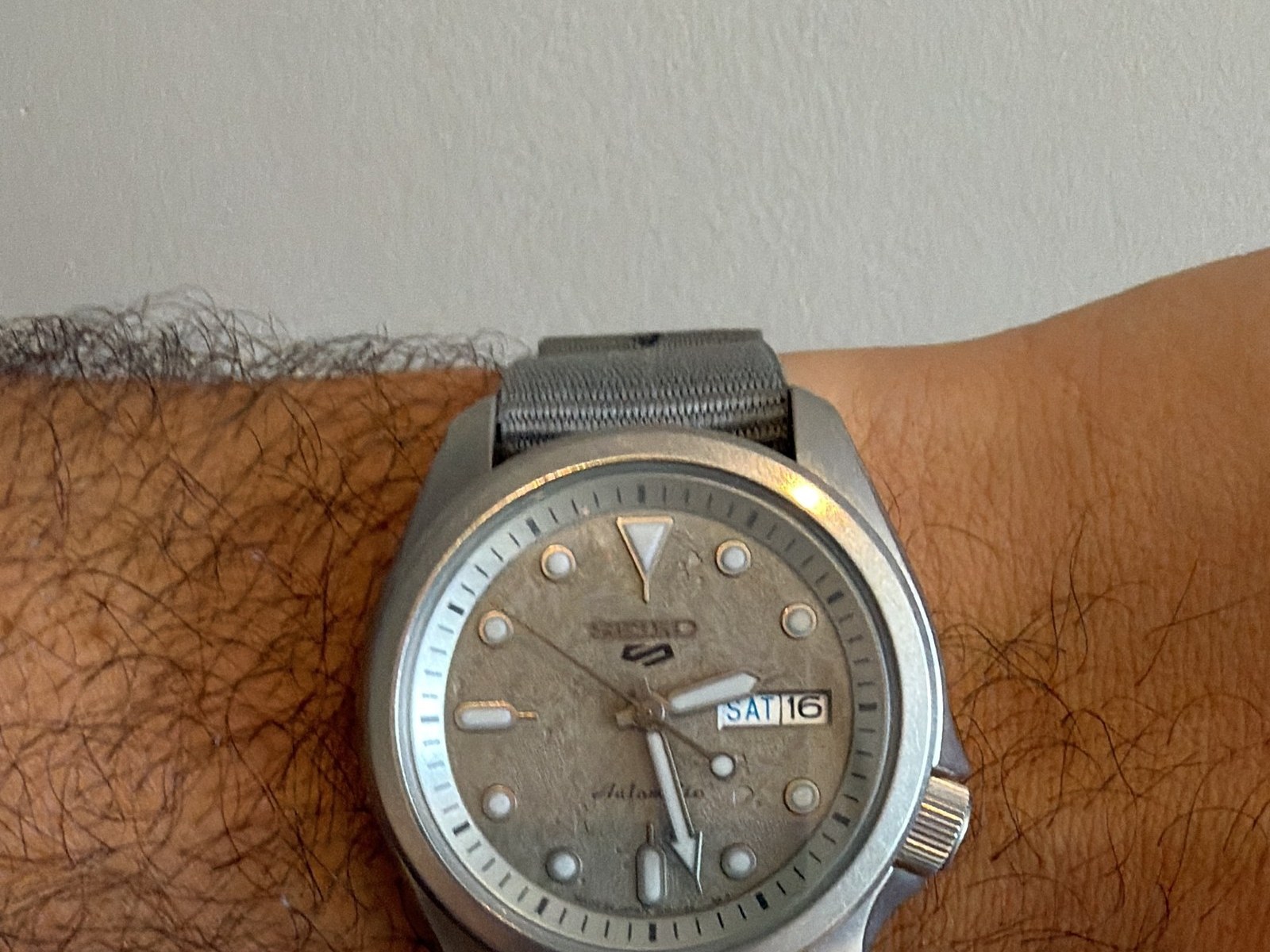 No pulso, com a pulseira de nylon cinza que veio de fábrica.